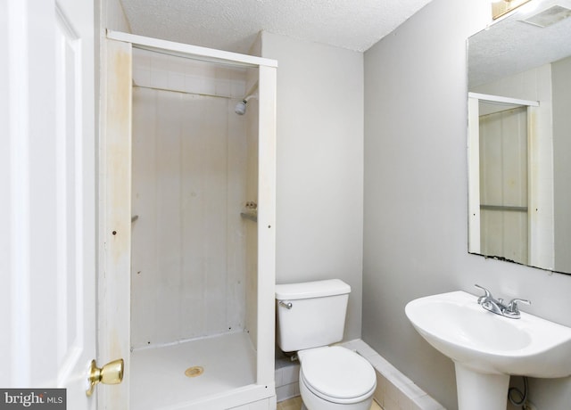 bathroom with a textured ceiling, a sink, a tile shower, and toilet