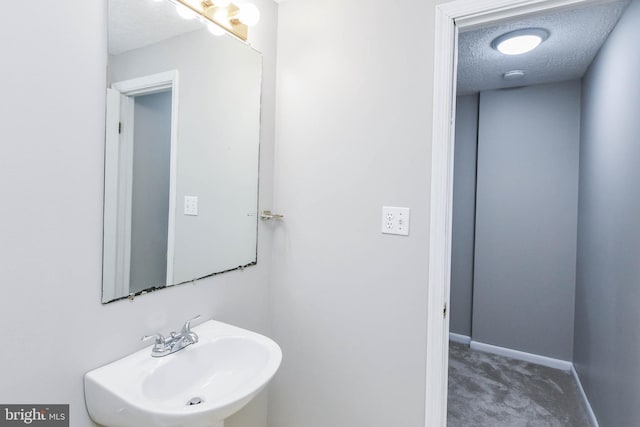 bathroom with a textured ceiling, baseboards, and a sink