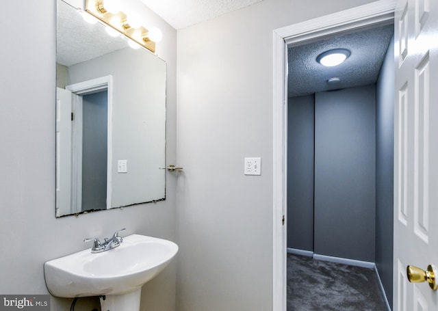 bathroom with a textured ceiling, a sink, and baseboards