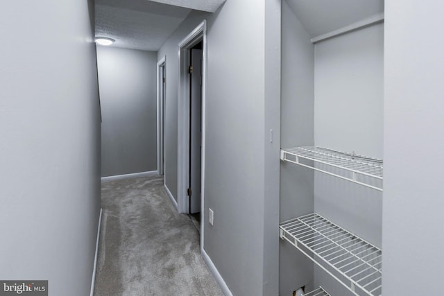 hallway with a textured ceiling, carpet flooring, and baseboards