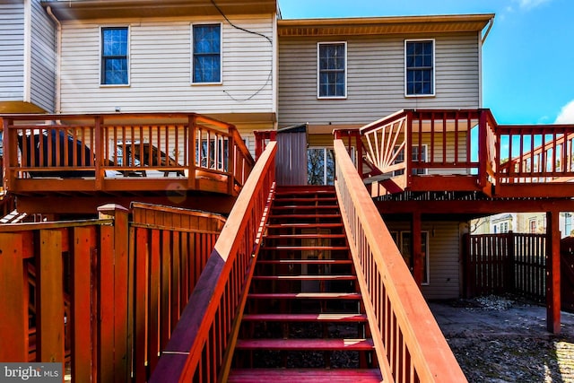 rear view of property featuring stairs, a wooden deck, and fence