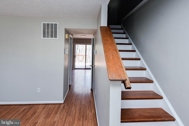 stairs with a textured ceiling, wood finished floors, visible vents, and baseboards