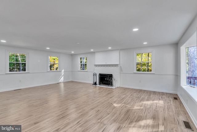 unfurnished living room with a fireplace, light wood-type flooring, and plenty of natural light