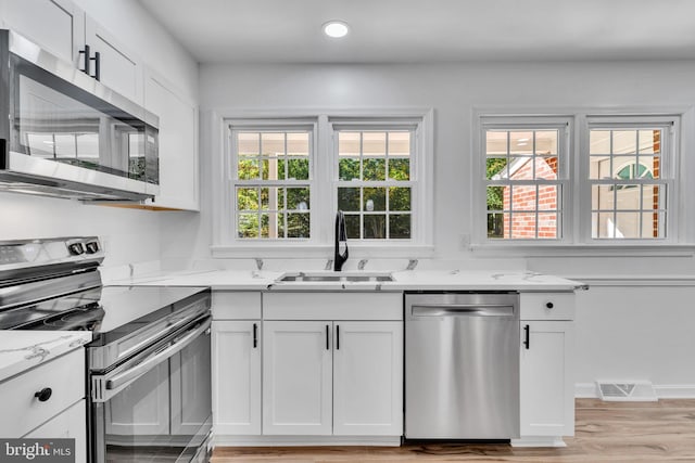 kitchen with stainless steel appliances, sink, white cabinetry, light stone counters, and light wood-type flooring