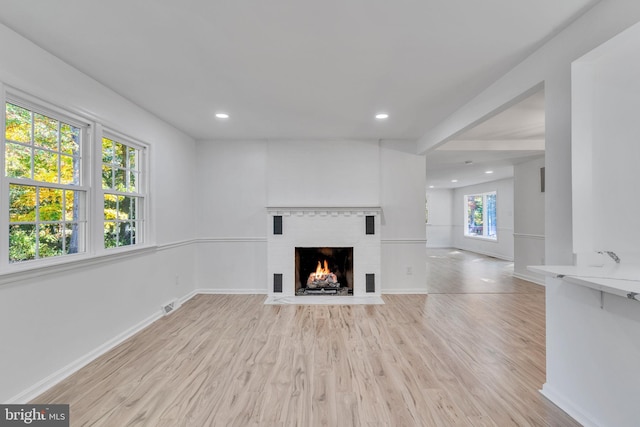 unfurnished living room featuring a brick fireplace, a wealth of natural light, and light hardwood / wood-style flooring