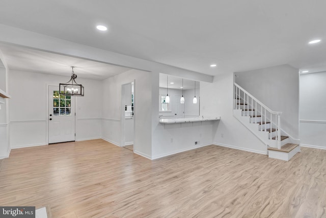 unfurnished living room featuring a notable chandelier and light wood-type flooring