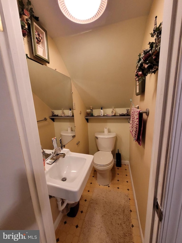 bathroom with toilet, tile patterned flooring, vaulted ceiling, and sink