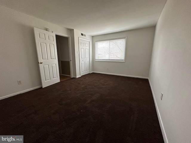 unfurnished bedroom with dark carpet and a closet