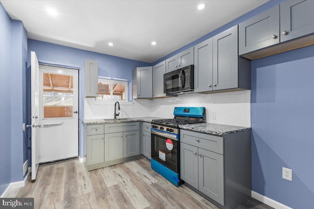 kitchen featuring sink, light stone counters, light wood-type flooring, backsplash, and stainless steel range with gas stovetop