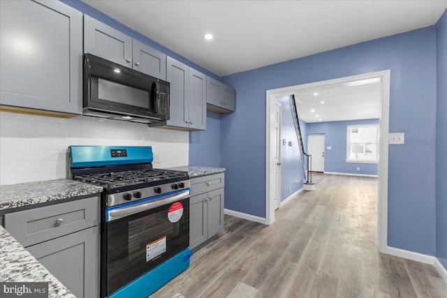 kitchen with light wood-type flooring, stainless steel gas range, light stone counters, and tasteful backsplash