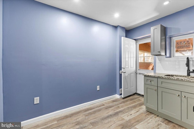 kitchen featuring sink, tasteful backsplash, light hardwood / wood-style floors, and light stone countertops