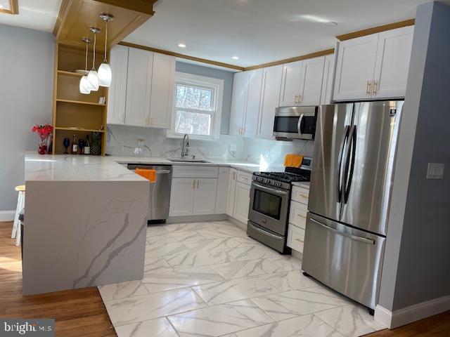 kitchen featuring white cabinets, kitchen peninsula, stainless steel appliances, and pendant lighting