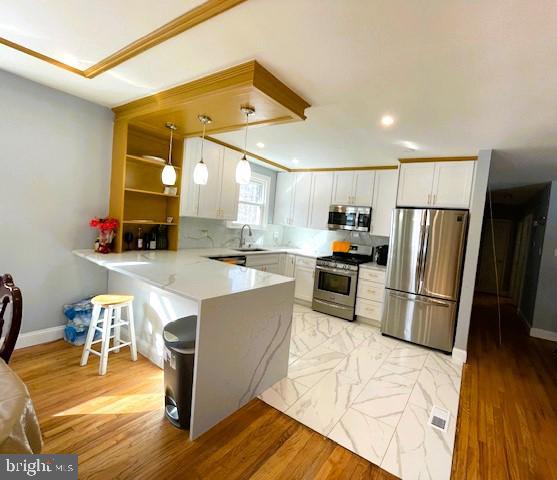 kitchen featuring pendant lighting, white cabinetry, appliances with stainless steel finishes, and kitchen peninsula