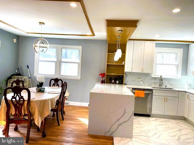 kitchen featuring tasteful backsplash, white cabinets, hanging light fixtures, stainless steel dishwasher, and light stone counters