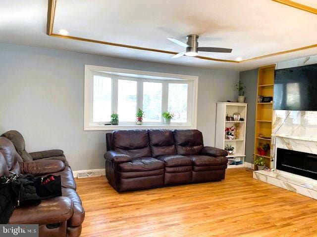 living room featuring a fireplace, built in shelves, ceiling fan, and light wood-type flooring