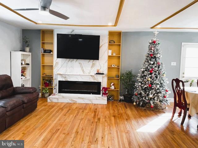 living room featuring ceiling fan, built in shelves, a high end fireplace, and hardwood / wood-style floors