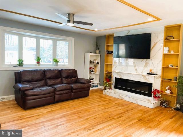 living room featuring light hardwood / wood-style floors, ceiling fan, built in shelves, and a stone fireplace