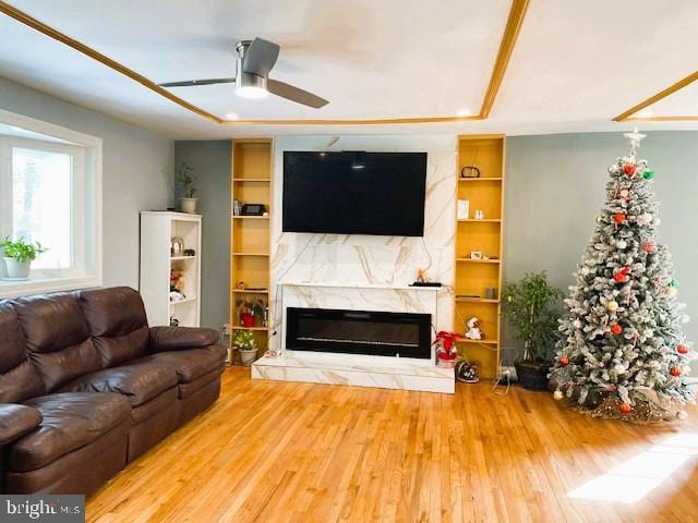 living room featuring ceiling fan, a fireplace, wood-type flooring, a tray ceiling, and built in features