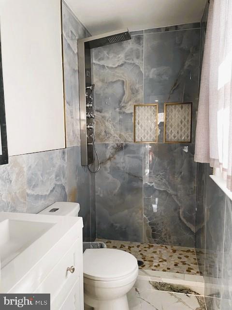 bathroom featuring toilet, a tile shower, tile walls, and vanity