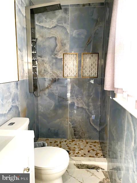 bathroom with toilet, vanity, tile walls, and tiled shower