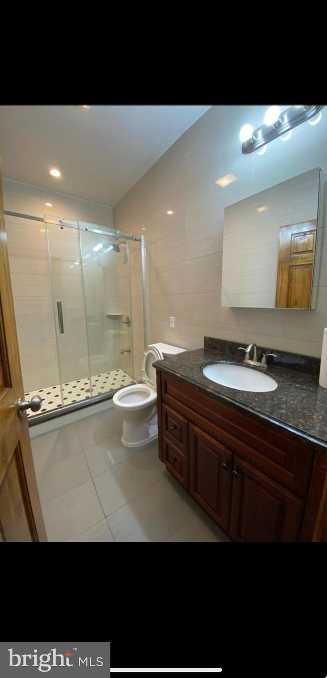 bathroom featuring toilet, tile patterned flooring, tile walls, an enclosed shower, and vanity