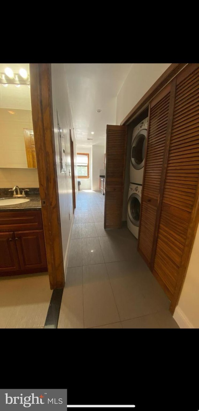 corridor with sink, stacked washing maching and dryer, and light tile patterned flooring