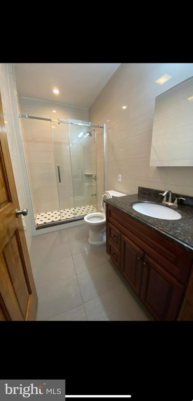 bathroom with toilet, walk in shower, vanity, tile patterned floors, and tile walls