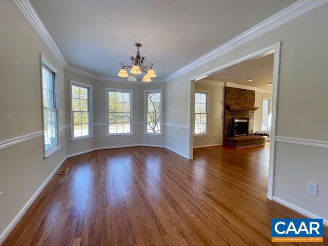 unfurnished dining area with a brick fireplace, crown molding, a healthy amount of sunlight, and an inviting chandelier