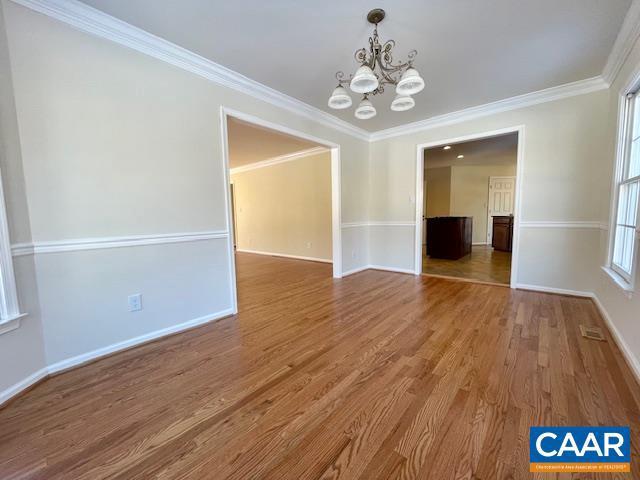 empty room featuring crown molding, hardwood / wood-style flooring, and a notable chandelier