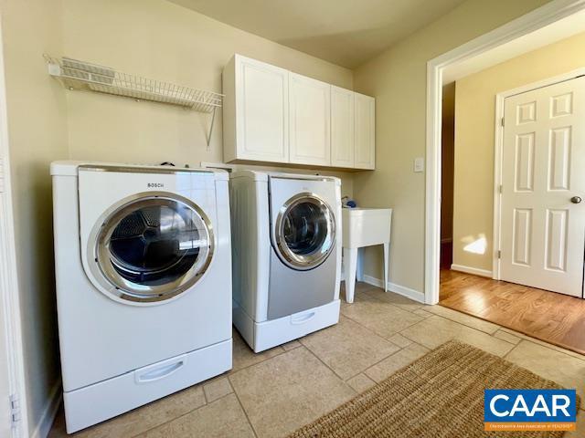 clothes washing area featuring light wood-type flooring, cabinets, and washer and clothes dryer