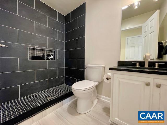 bathroom featuring toilet, vanity, and a tile shower