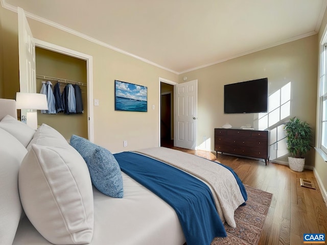 bedroom with a walk in closet, a closet, crown molding, and wood-type flooring