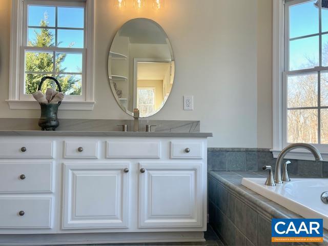 bathroom featuring a relaxing tiled tub and vanity