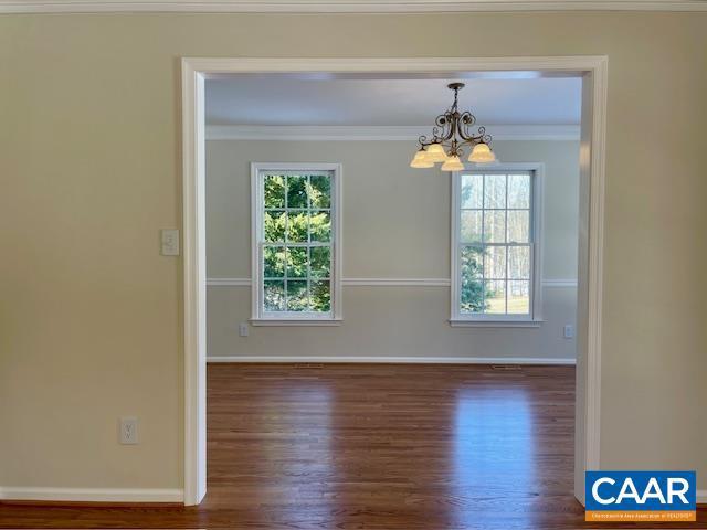 spare room featuring dark hardwood / wood-style flooring, crown molding, and an inviting chandelier