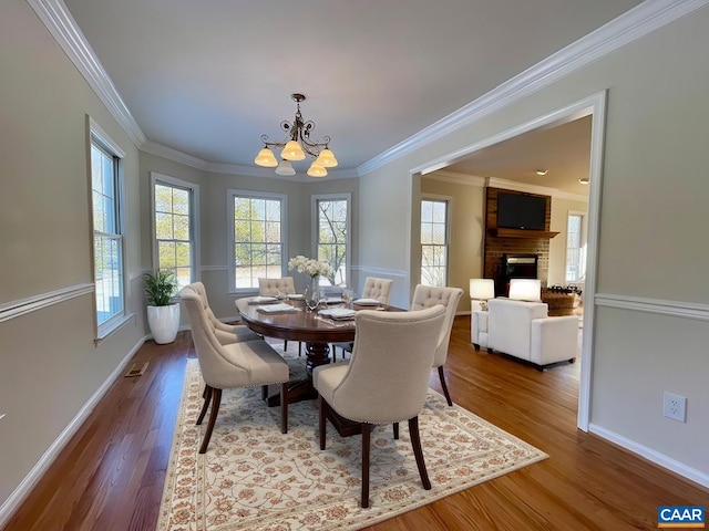 dining space with a brick fireplace, crown molding, a chandelier, and a healthy amount of sunlight