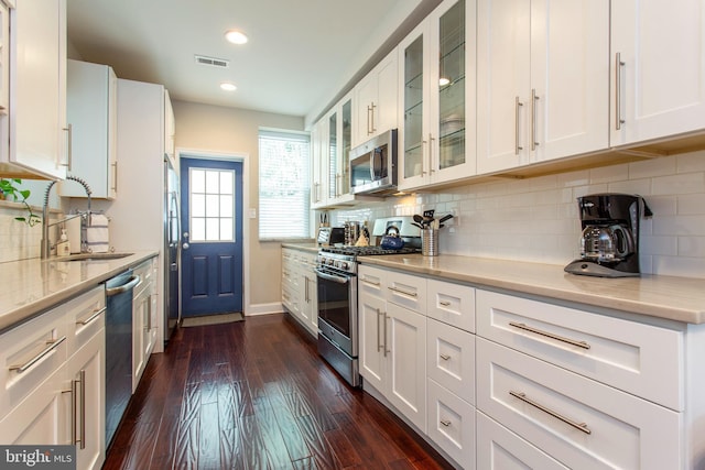 kitchen with light stone counters, dark wood-type flooring, backsplash, white cabinetry, and appliances with stainless steel finishes