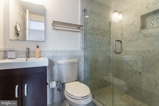 bathroom featuring tile walls, vanity, a shower with shower door, and toilet