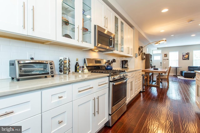 kitchen with appliances with stainless steel finishes, light stone counters, dark hardwood / wood-style floors, white cabinetry, and tasteful backsplash