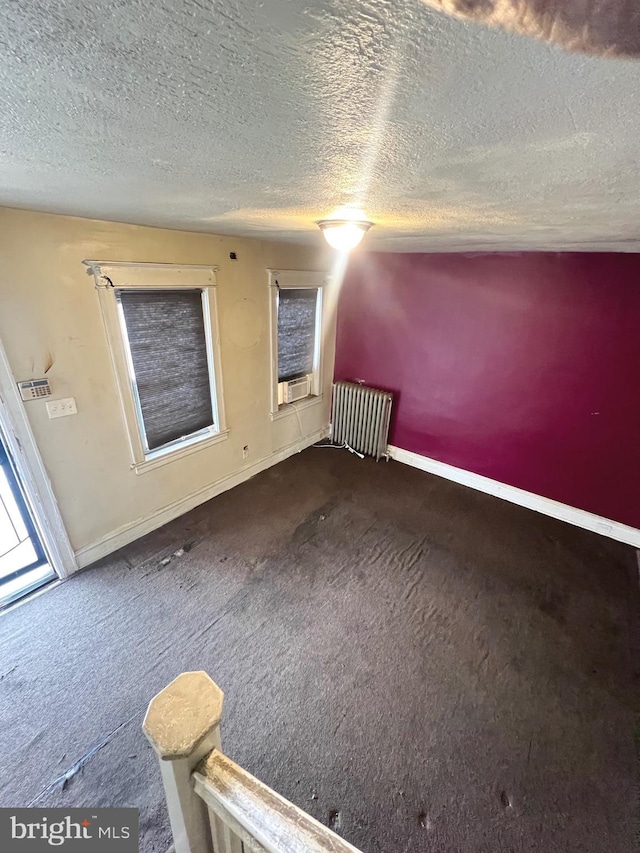 empty room featuring a textured ceiling, dark colored carpet, and radiator