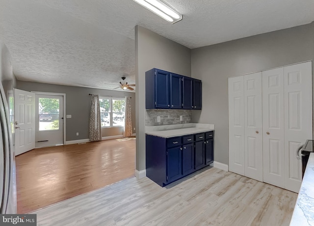 kitchen featuring tasteful backsplash, blue cabinetry, a textured ceiling, and light hardwood / wood-style floors