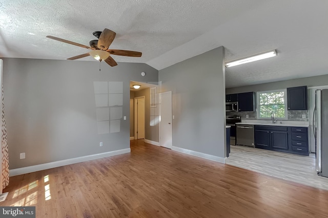 unfurnished living room featuring ceiling fan, light wood-type flooring, lofted ceiling, a textured ceiling, and sink