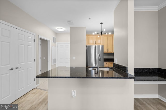 kitchen featuring crown molding, dark stone counters, stainless steel fridge, sink, and decorative light fixtures