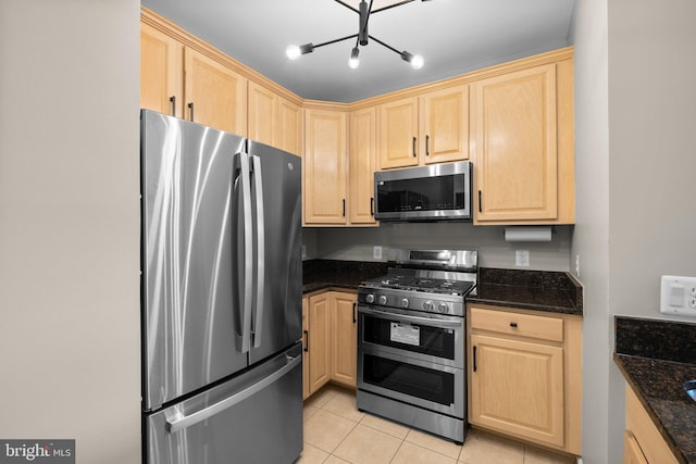 kitchen with stainless steel appliances, light brown cabinetry, light tile patterned floors, and dark stone counters