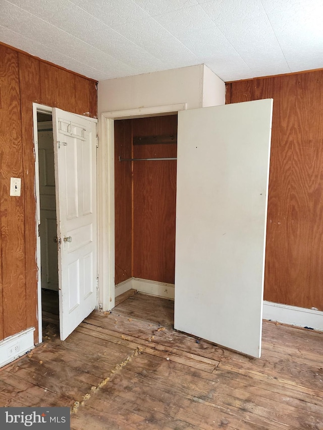 unfurnished bedroom featuring wooden walls, a closet, and dark hardwood / wood-style floors