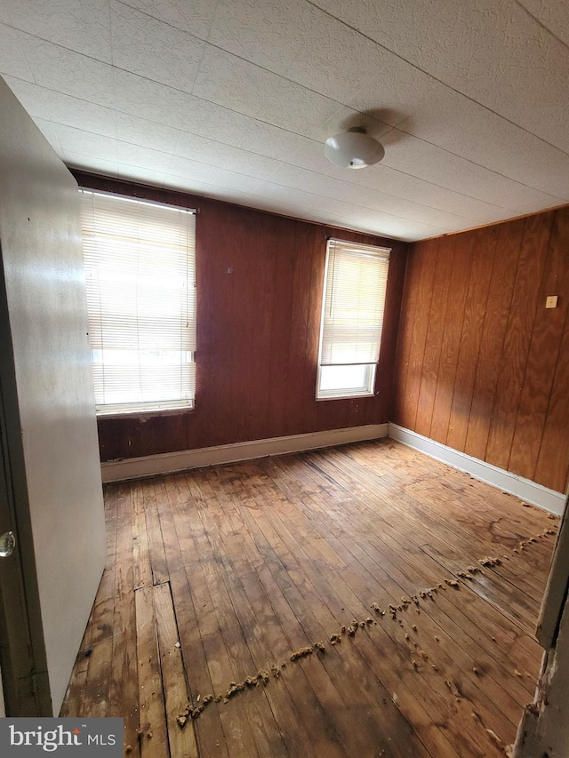 unfurnished room featuring a wealth of natural light, wood walls, and wood-type flooring