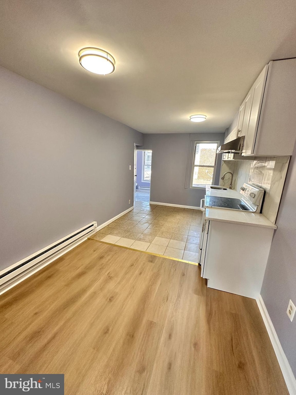 kitchen featuring tasteful backsplash, white cabinets, light hardwood / wood-style flooring, a baseboard radiator, and sink