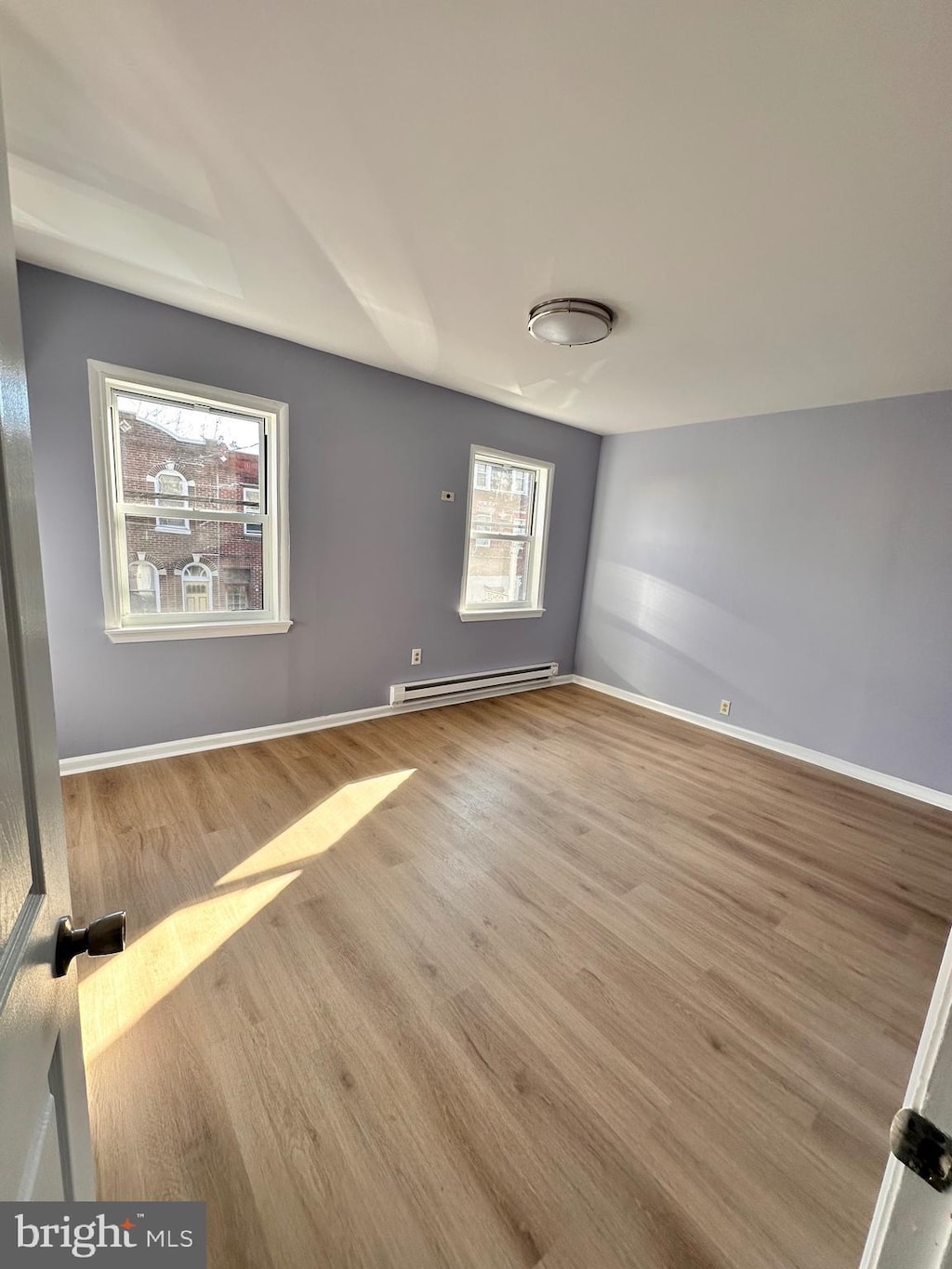 unfurnished room featuring baseboard heating and light wood-type flooring