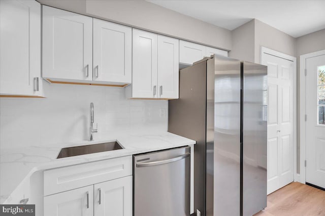 kitchen featuring white cabinets, stainless steel appliances, light stone countertops, sink, and light hardwood / wood-style flooring