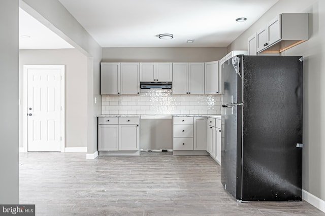 kitchen featuring black fridge, light wood-type flooring, gray cabinets, and tasteful backsplash