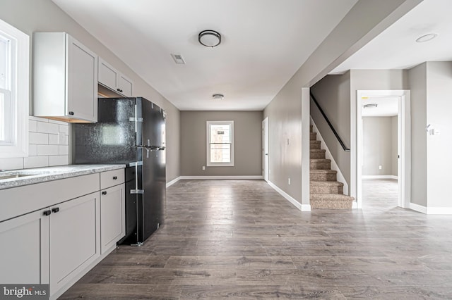 kitchen featuring dark wood-type flooring, black fridge, sink, white cabinetry, and backsplash